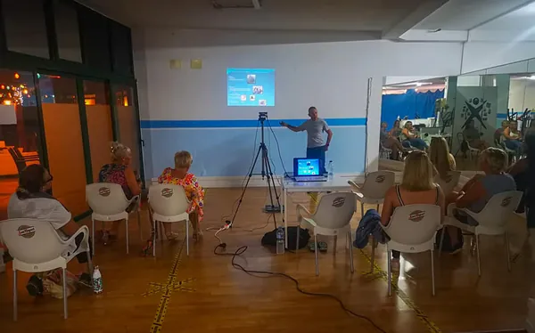 Charla de nutrición en un gimnasio, con el público sentado frente a la pantalla