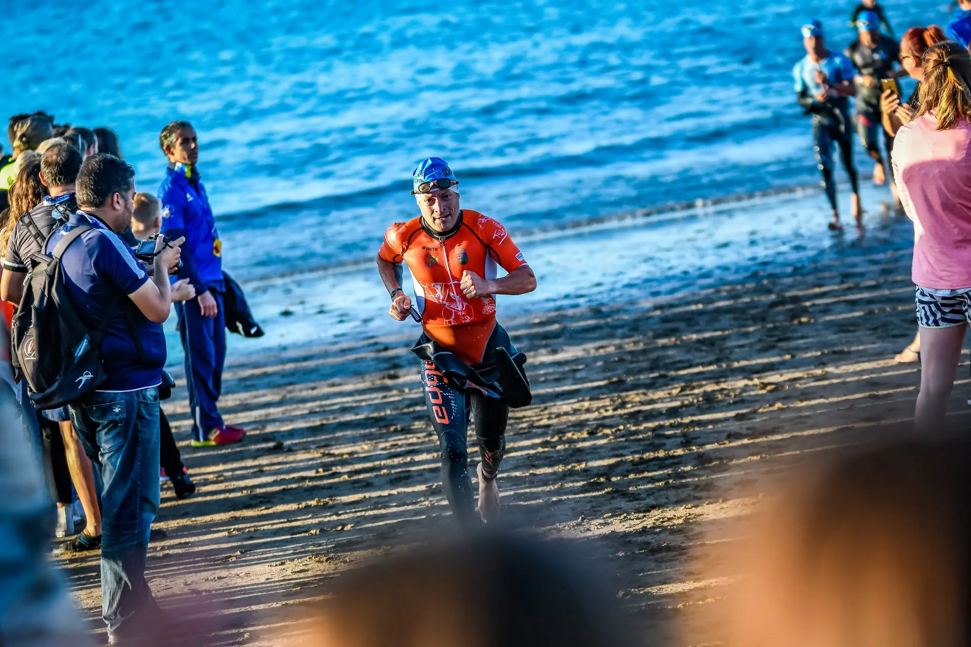 Fran Delgado saliendo del mar en un triatlón, con el mono naranja, entre el público de la playa