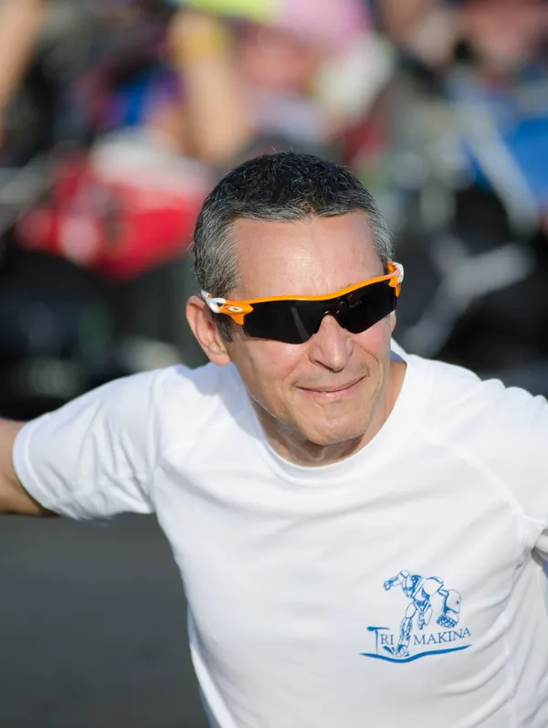Fran Delgado sonriendo, con gafas de sol naranjas y la camiseta blanca del equipo Tri Makina