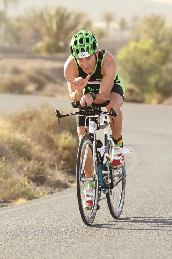 Triatleta con casco verde en bicicleta por una carretera de Lanzarote