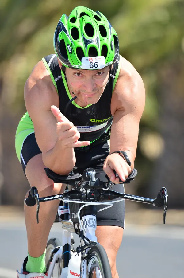 Triatleta con casco verde, acoplado en su bicicleta de contrarreloj, saludando a la cámara