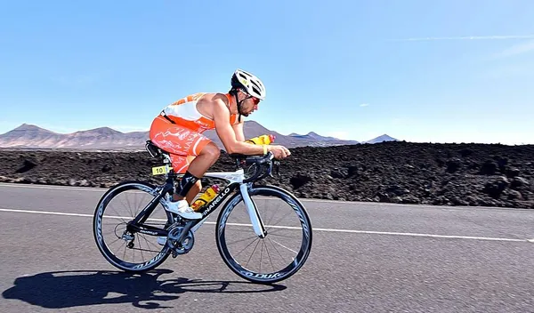 Triatleta con la equipación naranja en bicicleta, entre los campos de lava de Lanzarote