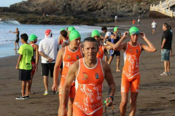 Triatletas del equipo saliendo del agua en una playa de arena oscura