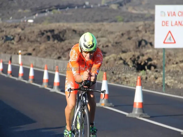 Fran Delgado en bicicleta de contrarreloj, con el mono naranja, por una carretera entre conos