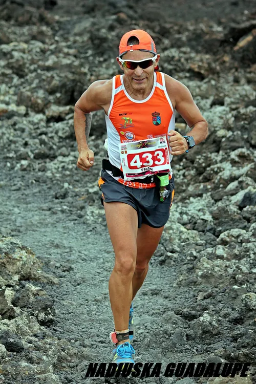 Corredor de trail con la camiseta naranja bajando por un terreno volcánico
