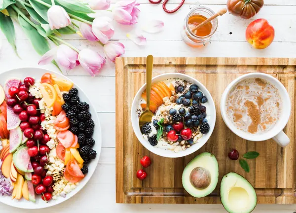 Cuencos de fruta fresca, frutos rojos y aguacate sobre una mesa de madera